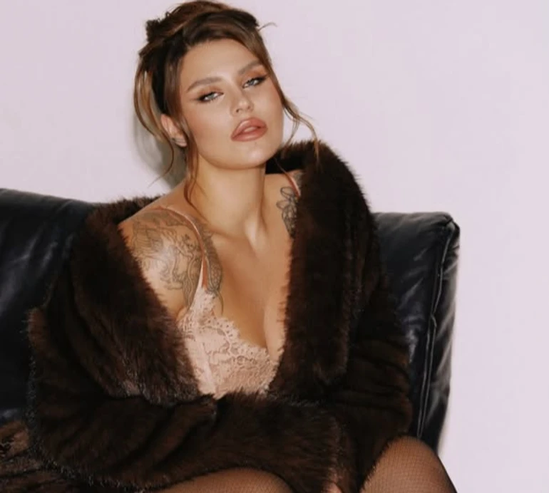 Млосна Заріцька в шубі та сукні-комбінації поспокушала ніжками на шкіряному кріслі. Фото