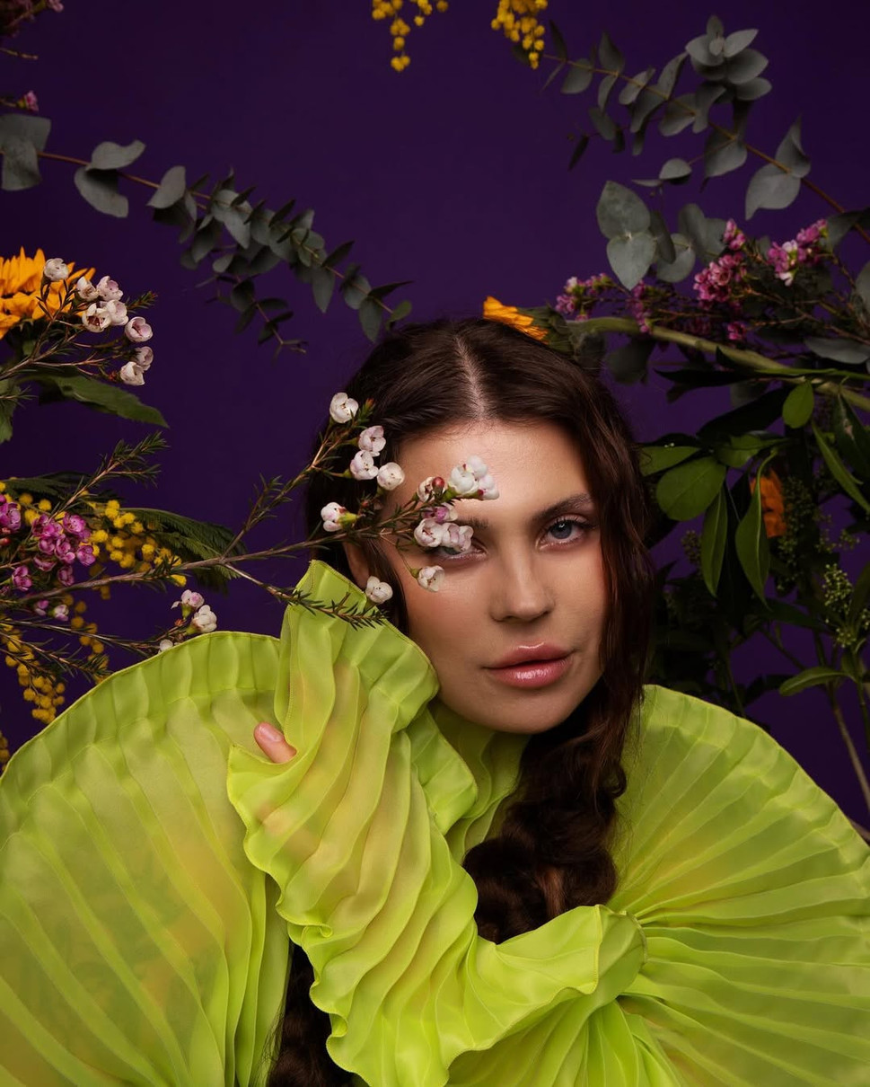 Олександра Заріцька одягнена у зелену сукню позує у квітах