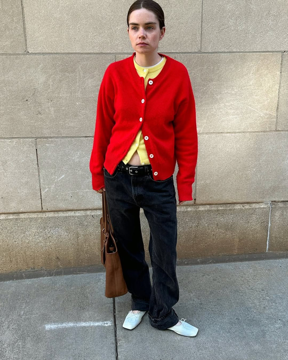 Дівчина на тлі стіни у подвійному кардигані