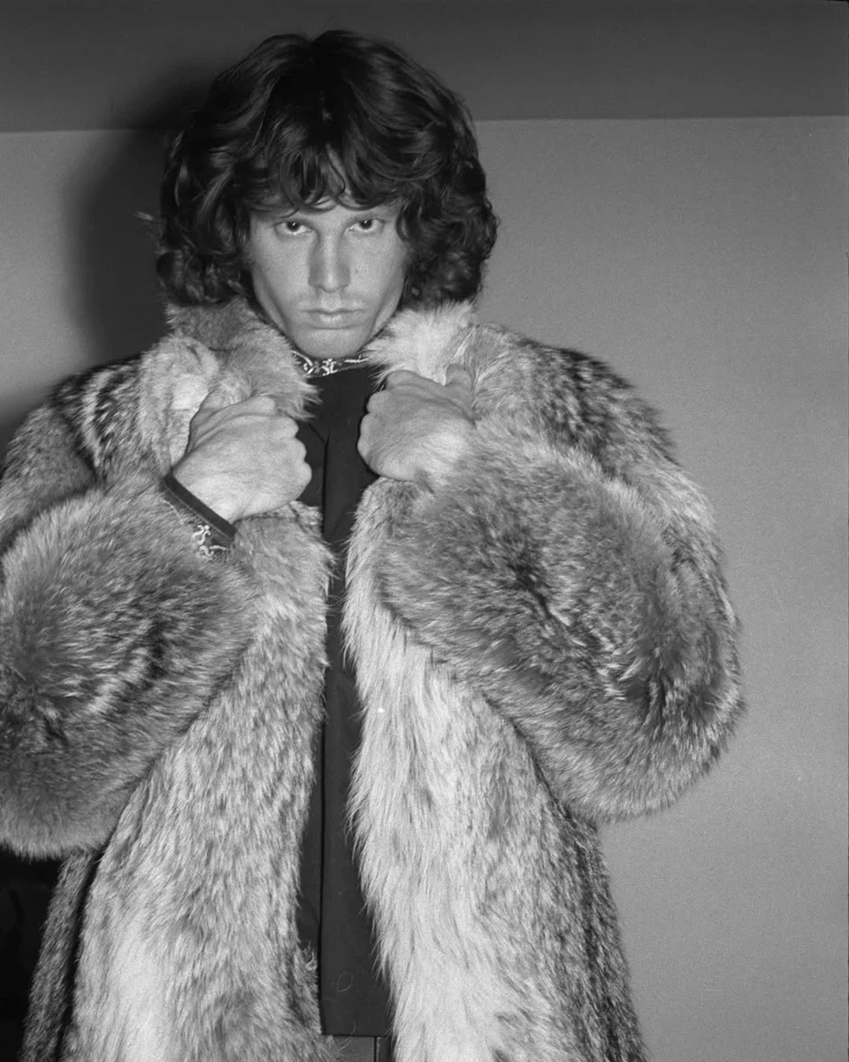 Джим Моррісон у шубі позує на фоні стіни